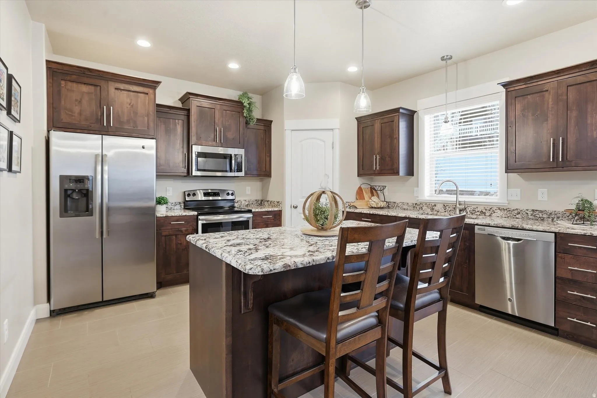 Kitchen with stainless steel appliances, light stone counters, dark wood finish cabinetry, a kitchen island, and a breakfast bar