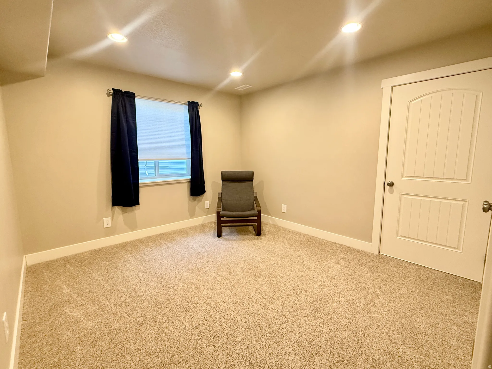 Neutral-toned carpeting, recessed ceiling lighting, and a single window with blinds