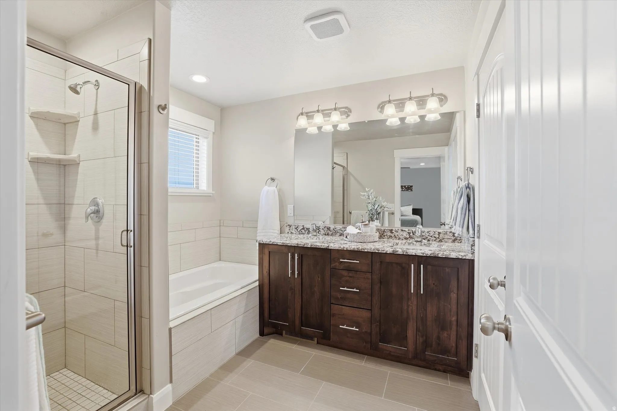Full bathroom with double vanity, a garden tub, a stall shower, light tile patterned flooring, and ensuite bath