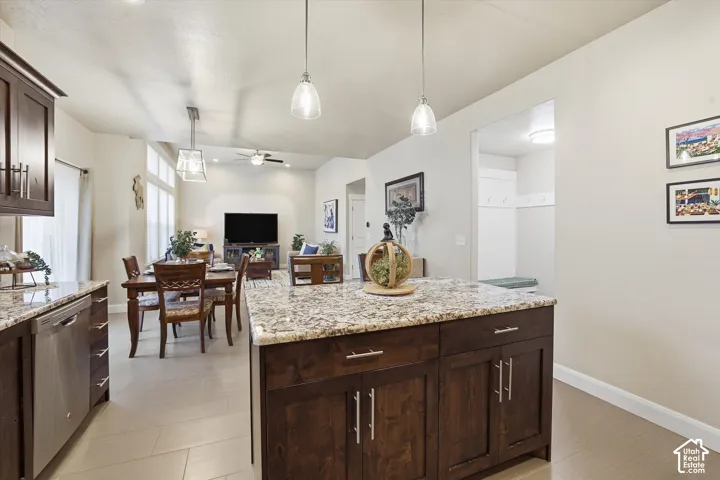 Kitchen with dark wood finish cabinets, dishwasher, light stone countertops, hanging light fixtures, and a ceiling fan