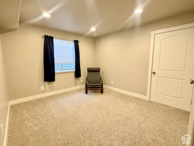 Neutral-toned carpeting, recessed ceiling lighting, and a single window with blinds