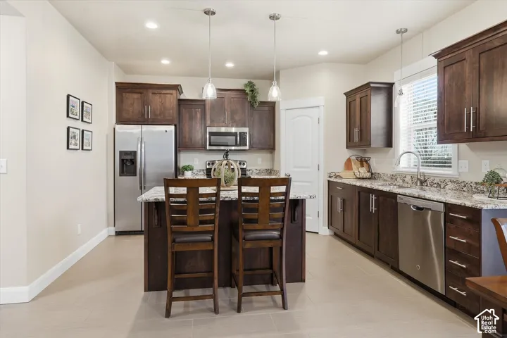 Kitchen featuring stainless steel appliances, dark wood finish cabinetry, light stone counters, and an island with sink