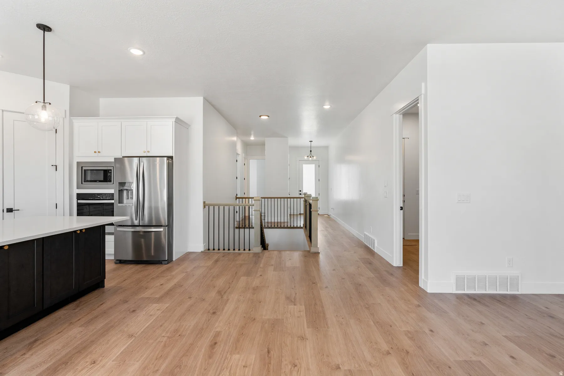 Dual tone kitchen featuring stainless steel appliances, dual tone cabinetry, hanging light fixtures, light wood finished floors, and light stone countertops