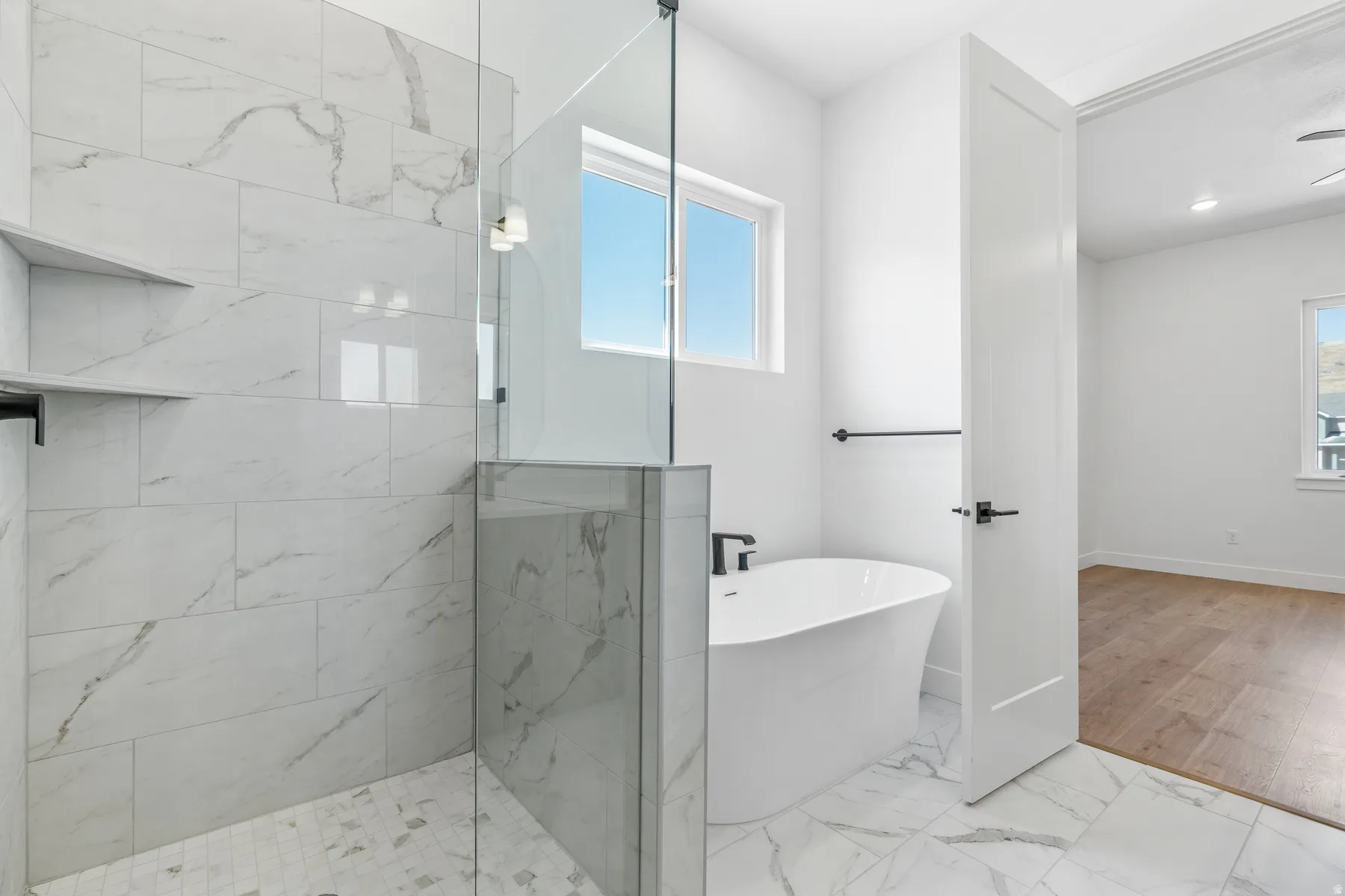 Full bath with a freestanding tub, light marble finish floors, and a marble finish shower