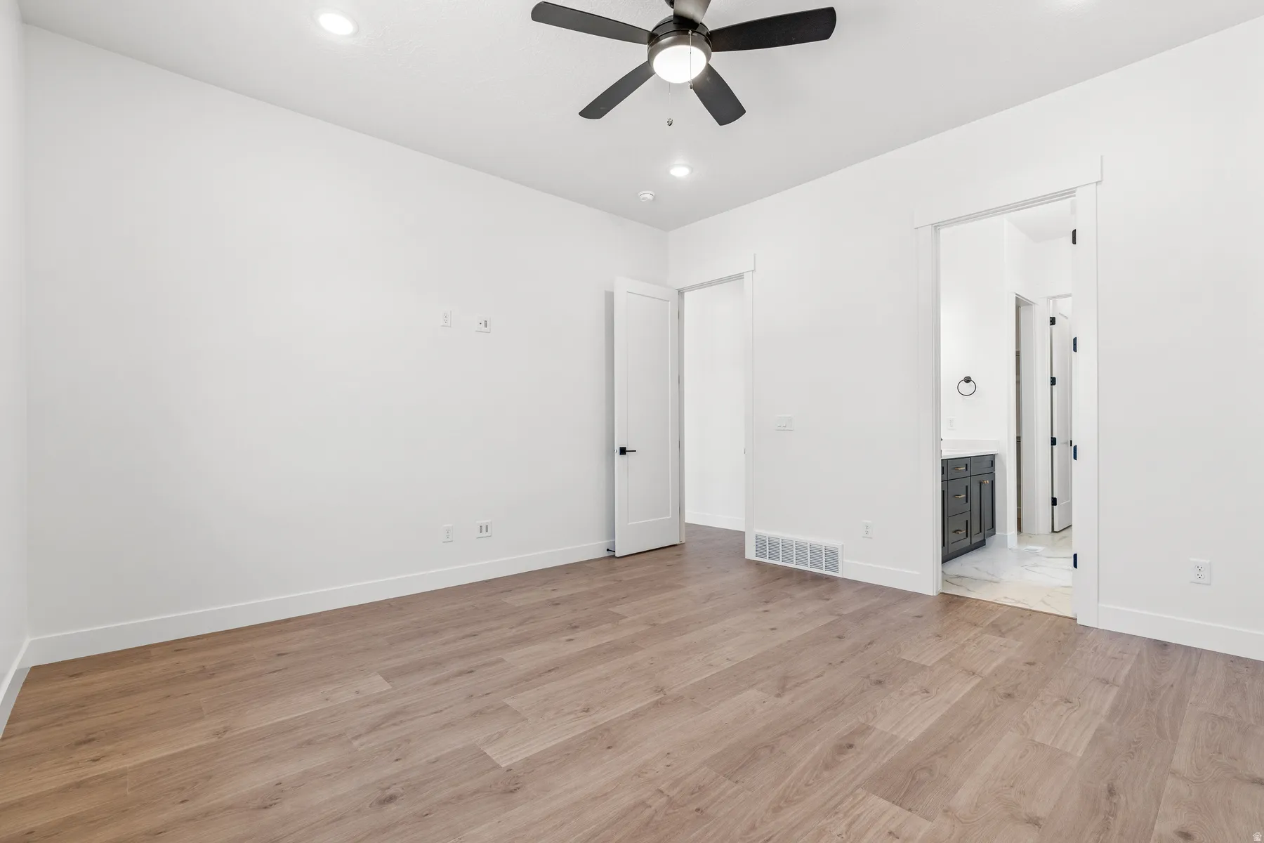 Unfurnished bedroom featuring light wood finished floors, a ceiling fan, ensuite bath, and recessed lighting