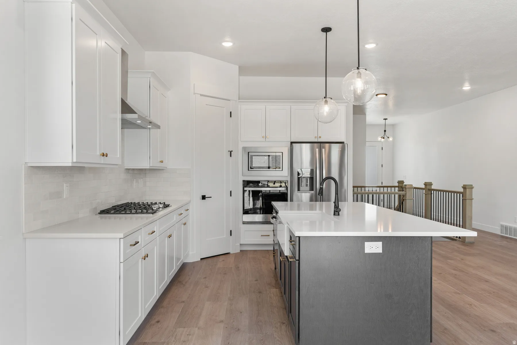 Kitchen featuring two tone cabinets, stainless steel appliances, a center island with sink, light wood finished floors, and decorative light fixtures