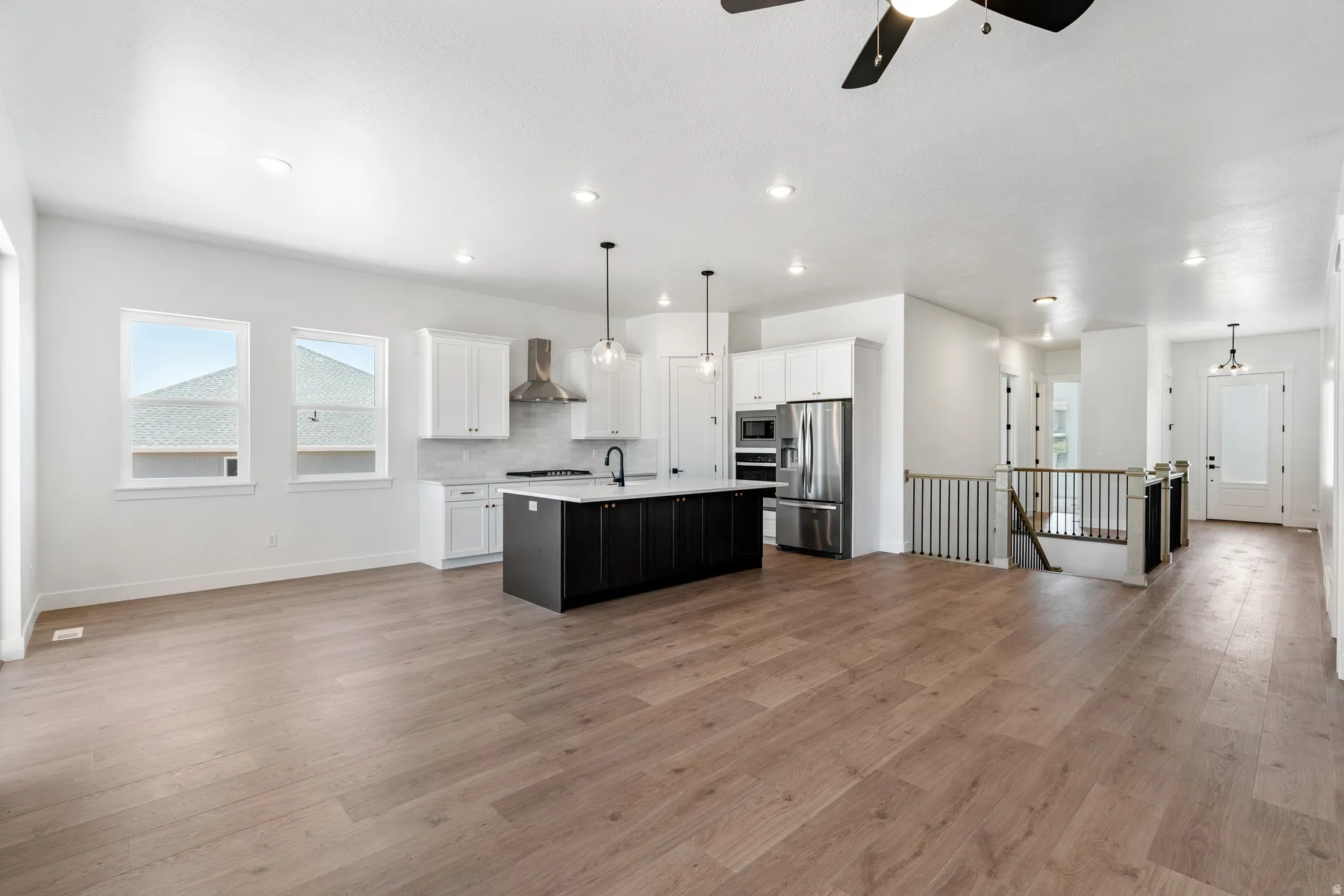 Two tone kitchen with an island with sink, stainless steel appliances, open floor plan, pendant lighting, and dual tone cabinetry