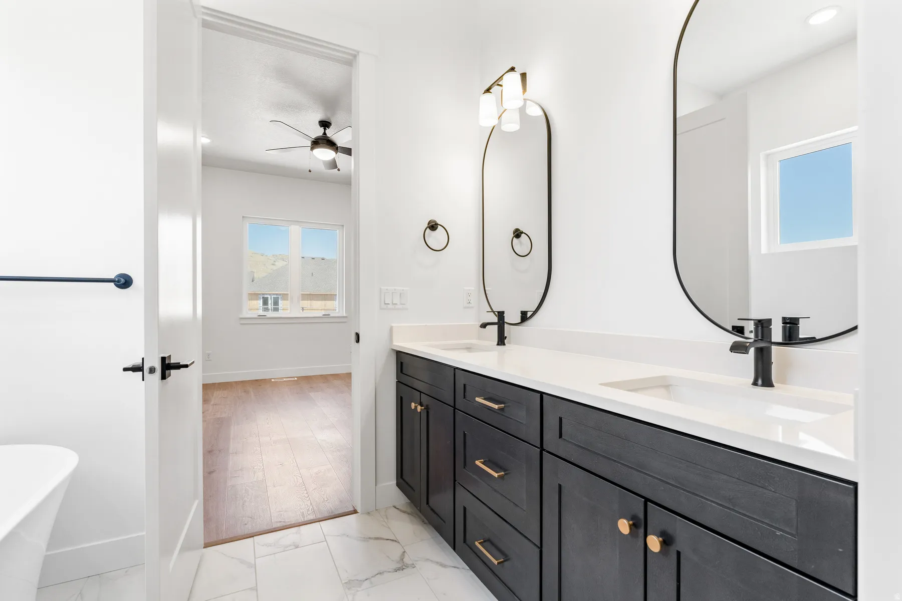 Bathroom featuring a freestanding bath, light marble finish floors, double vanity, a ceiling fan, and recessed lighting