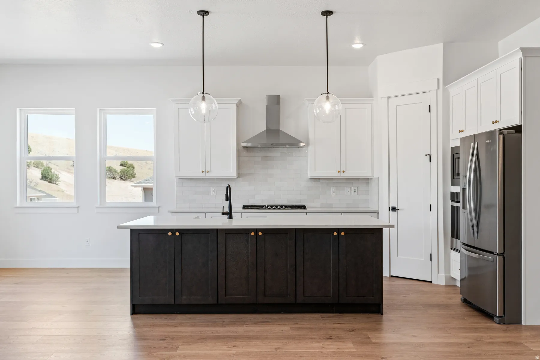 Dual tone kitchen with stainless steel appliances, a center island with sink, dual tone cabinets, pendant lighting, and light wood-type flooring