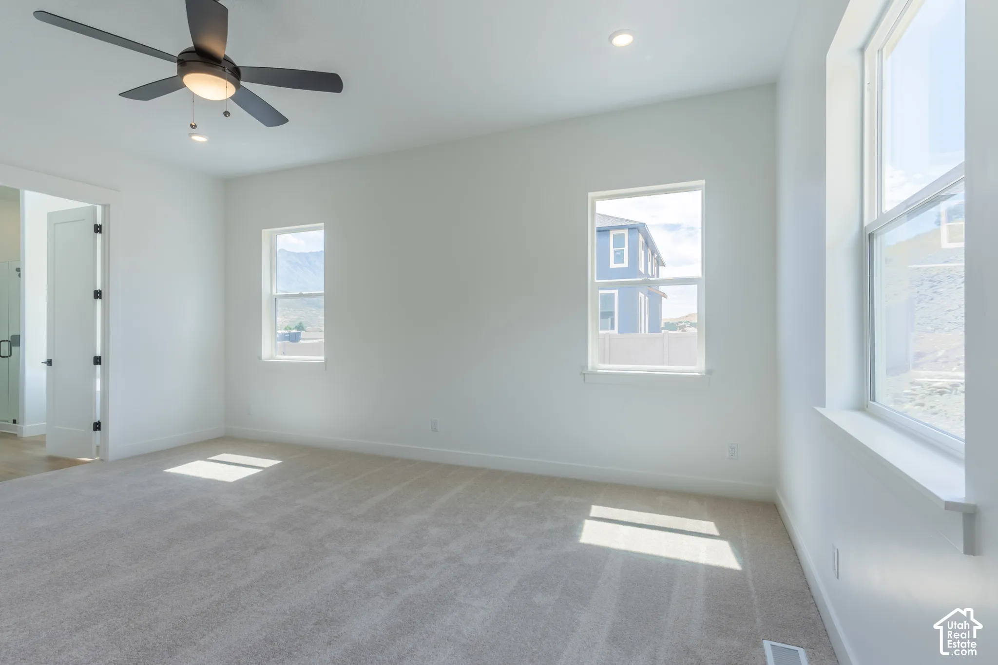 Spacious room featuring carpeting, multiple windows, a ceiling fan with integrated lighting, and recessed ceiling lights