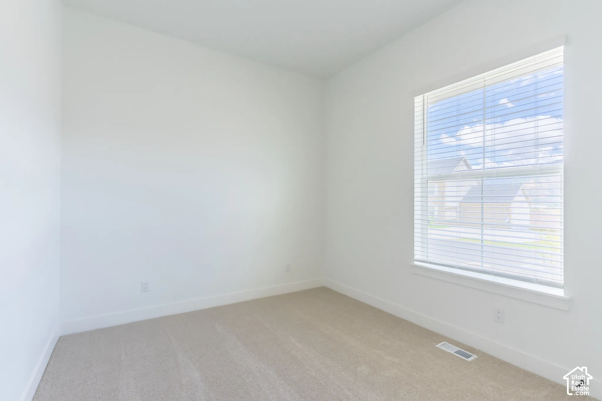 Bright corner bedroom with expansive window featuring plantation shutters, light wood-finish flooring, and pristine white walls ideal for personalization