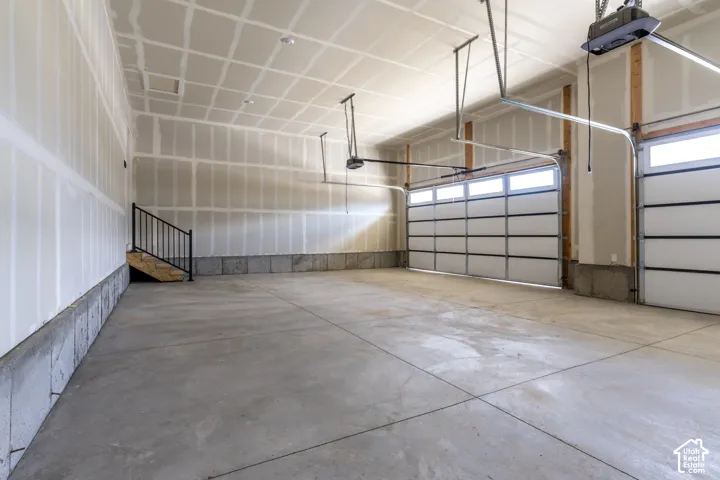 Spacious garage featuring two overhead doors with transom windows, a concrete floor, and access stairs with a metal railing