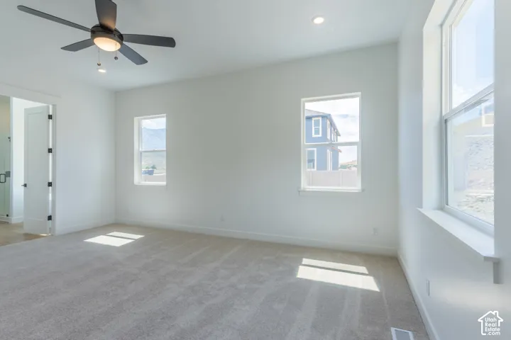 Spacious room featuring carpeting, multiple windows, a ceiling fan with integrated lighting, and recessed ceiling lights