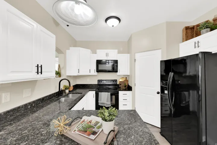 Modern kitchen featuring white shaker cabinetry, dark granite-style countertops, stainless steel undermount sink with a matte black faucet, black appliances including a microwave, and a black refrigerator