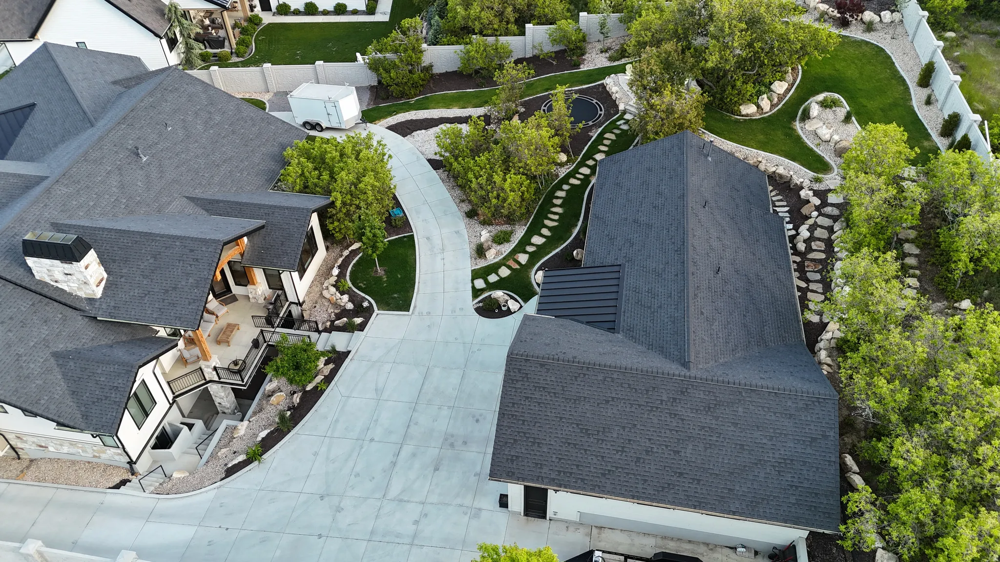 Expansive property featuring a large concrete driveway, a stone pathway, mature landscaping, and an outdoor patio with a built-in fireplace