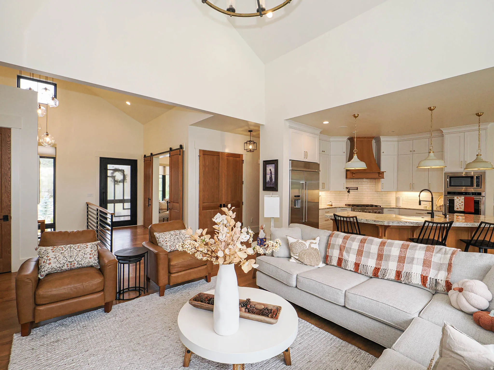 Living area featuring a barn door, vaulted ceiling, suspended lighting, and wood finished floors