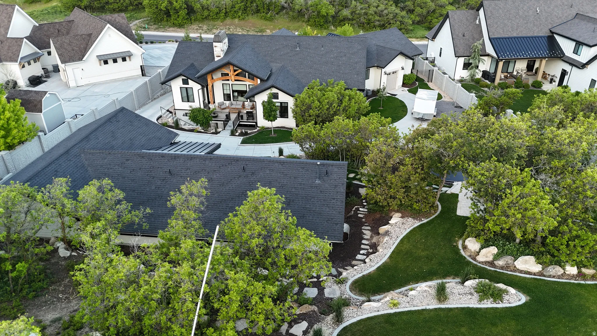 Expansive estate featuring a large main residence, manicured lawns, mature landscaping, a secondary structure with a dark roof, and a paved driveway