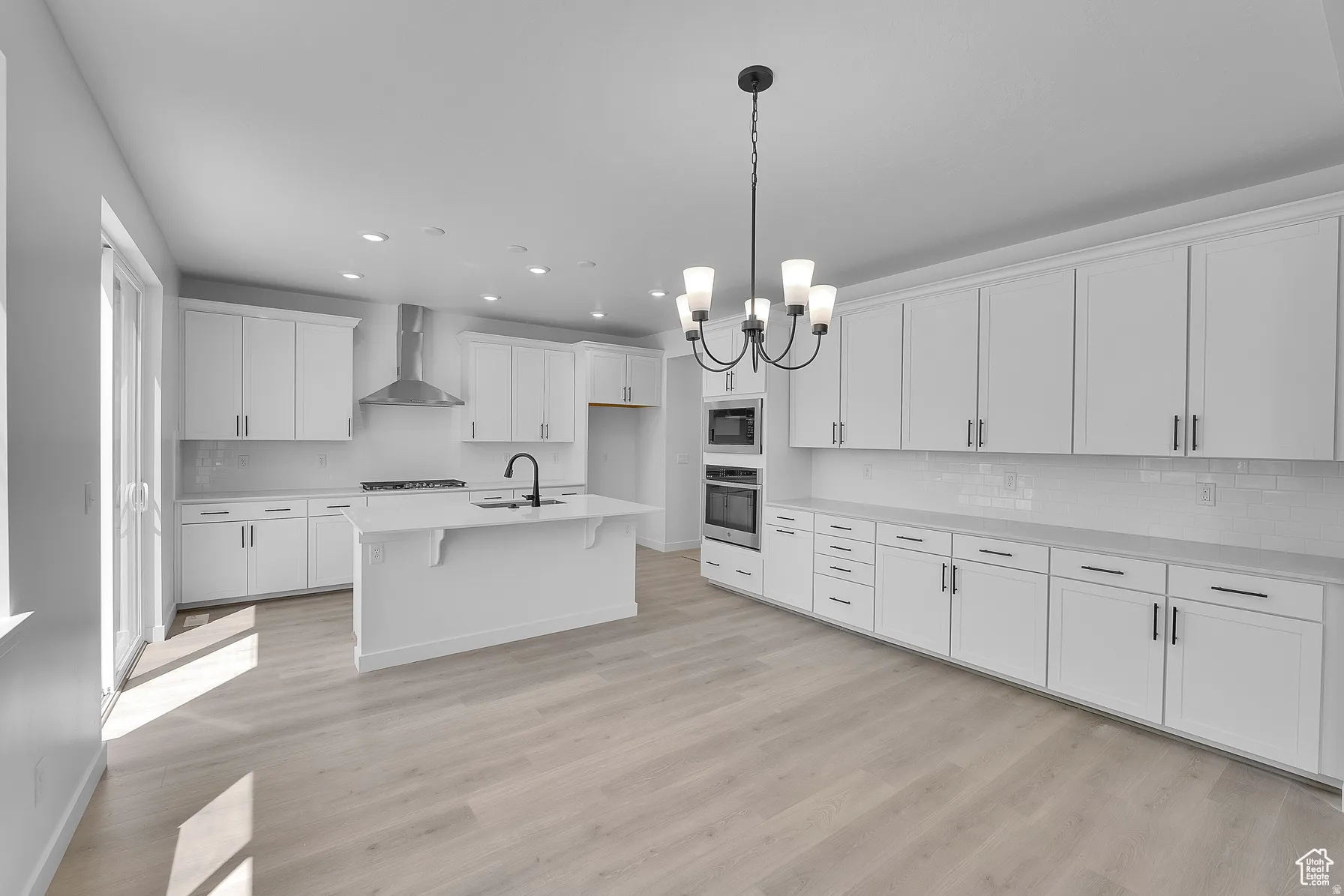 *Colors may vary** Kitchen featuring hanging lights, white cabinets, light wood finished floors, a kitchen breakfast bar, and a kitchen island with sink