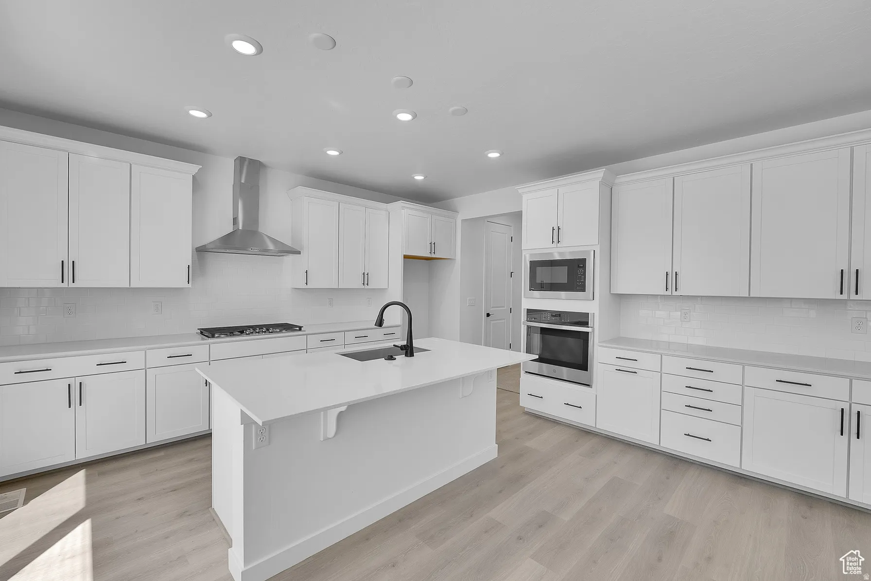 *Colors may vary** Kitchen featuring tasteful backsplash, light wood-type flooring, white cabinets, stainless steel appliances, and recessed lighting