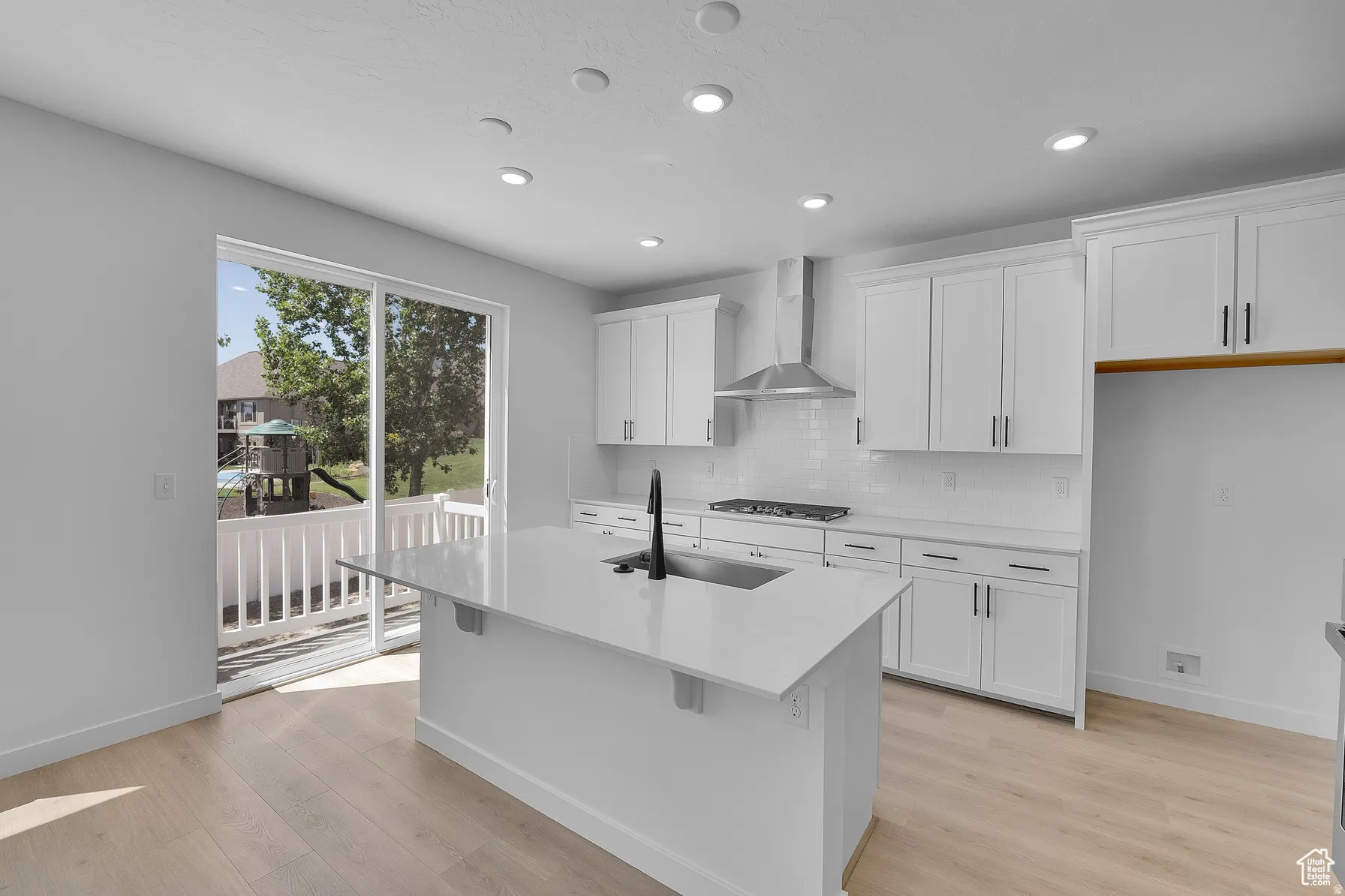 *Colors may vary** Kitchen featuring white cabinets, light stone counters, an island with sink, light wood-style floors, and recessed lighting