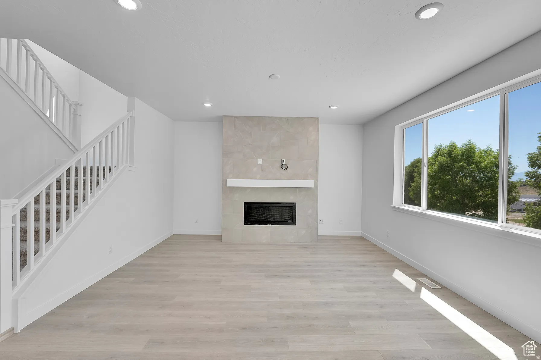 *Colors may vary** Unfurnished living room with light wood-type flooring, a tile fireplace, and recessed lighting