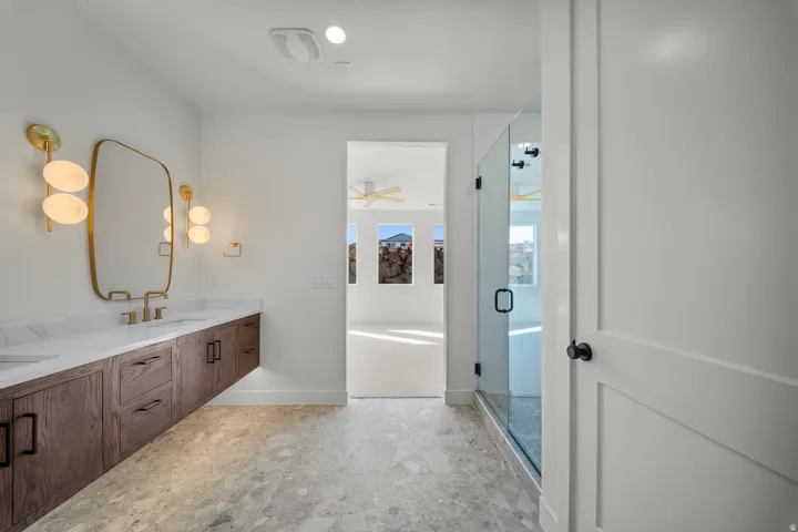 Full bathroom featuring double vanity, a shower stall, and ceiling fan