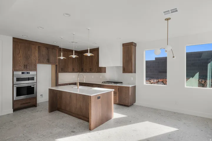 Kitchen with stainless steel appliances, decorative light fixtures, a kitchen island with sink, light stone counters, and decorative backsplash