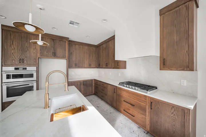 Kitchen featuring light stone counters, stainless steel appliances, tasteful backsplash, and decorative light fixtures