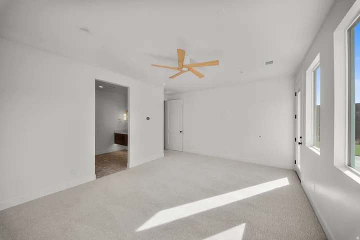 Empty room with light colored carpet and a ceiling fan