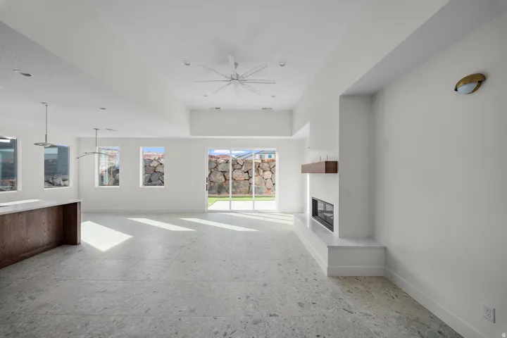 Unfurnished living room with plenty of natural light, a glass covered fireplace, and ceiling fan