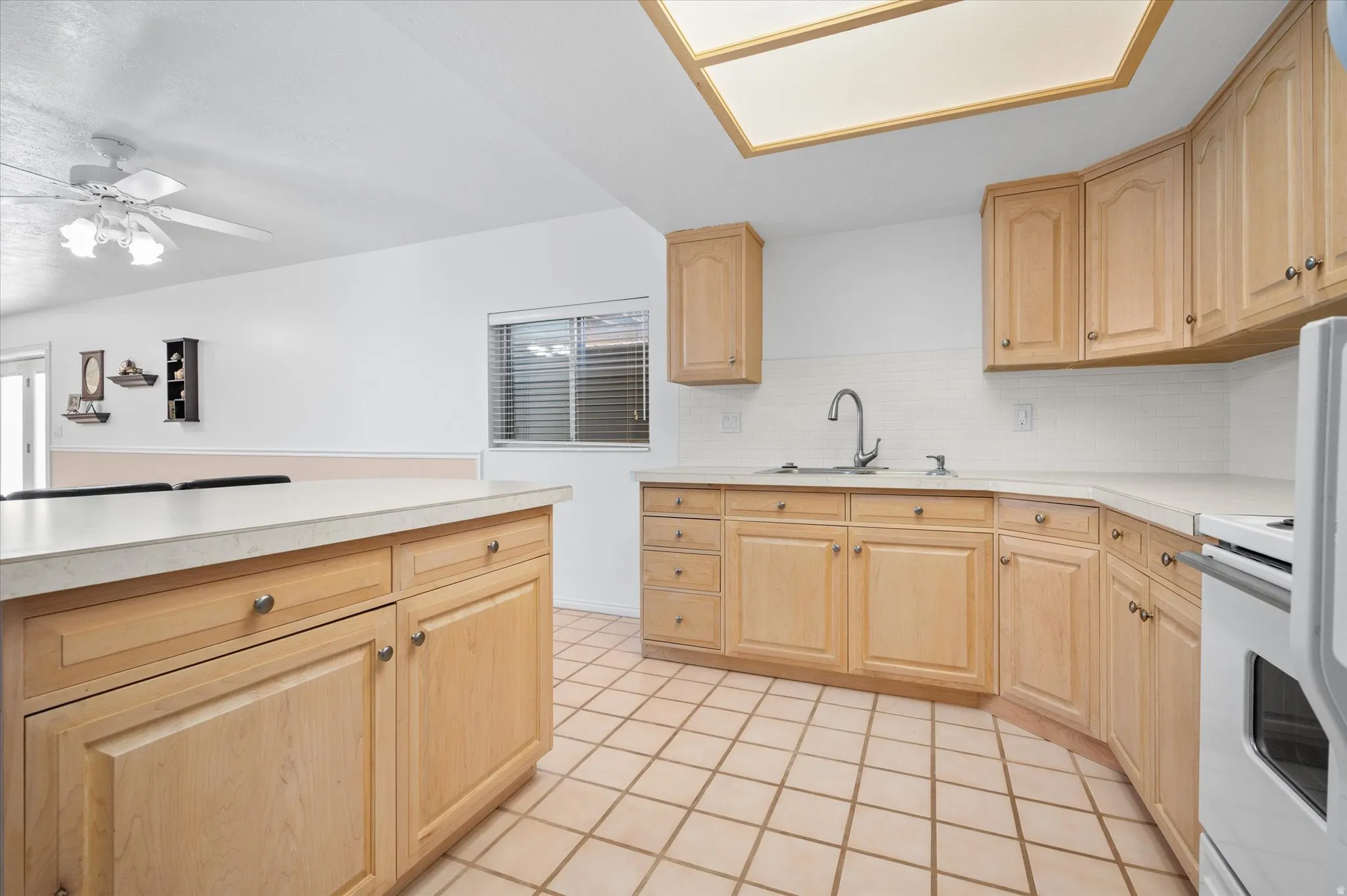 Kitchen featuring light wood finish cabinetry, light countertops, white stove, decorative backsplash, and a ceiling fan