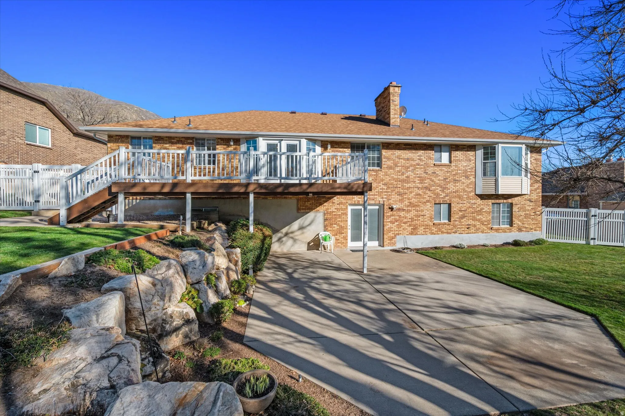 Back of property featuring a chimney, brick siding, a wooden deck, a patio,
