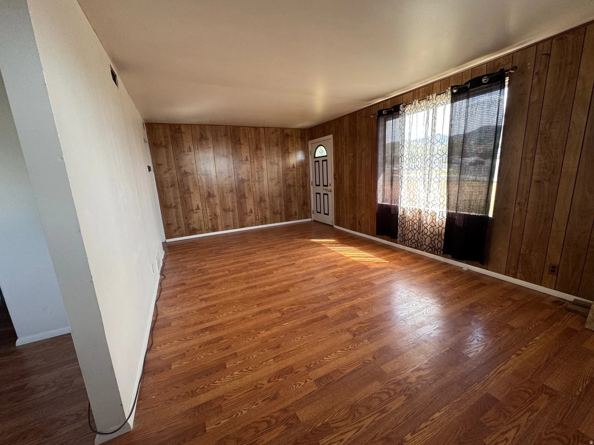 Spacious room featuring wood-finish flooring, wood paneling, a white entry door with rectangular window inserts, and white baseboards
