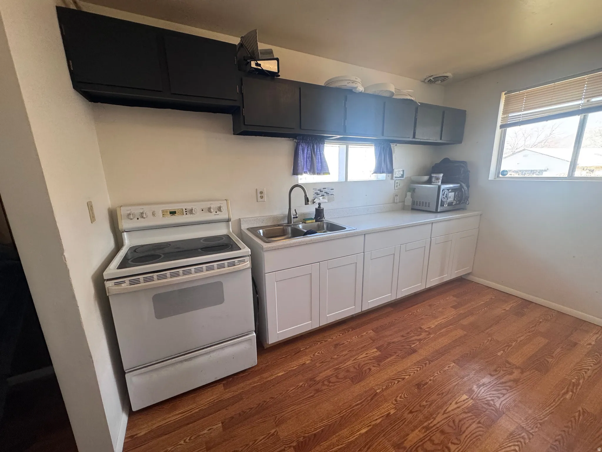 Kitchen with white range with electric stovetop, light countertops, dark wood-style floors, stainless steel microwave, and white cabinets