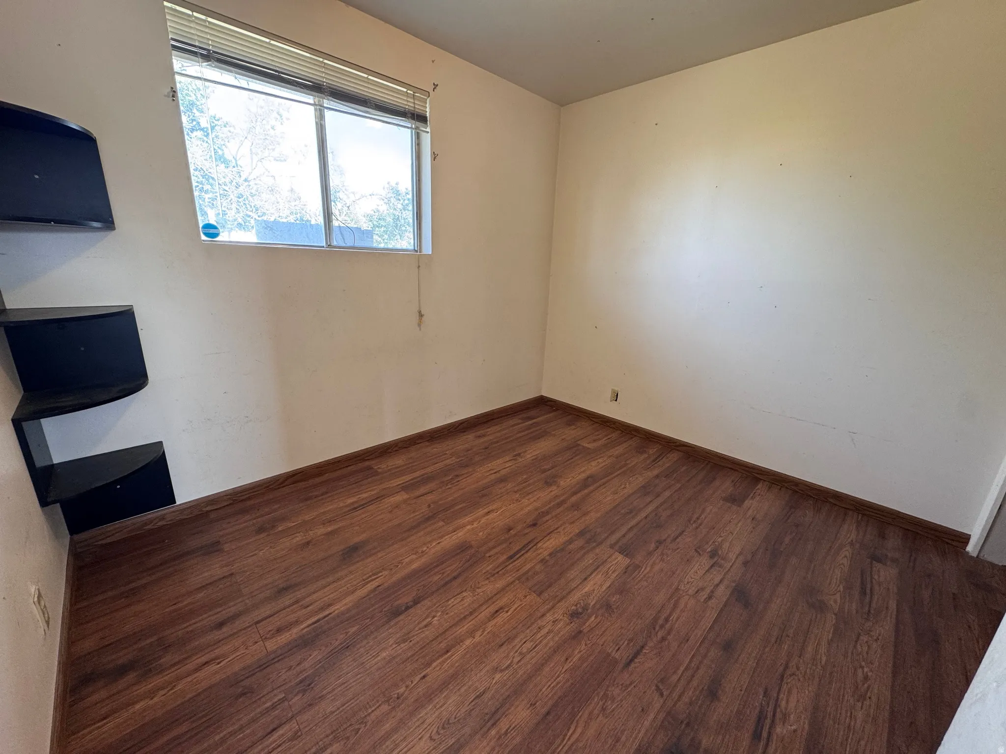 Room featuring wood-finish flooring and a window with horizontal blinds