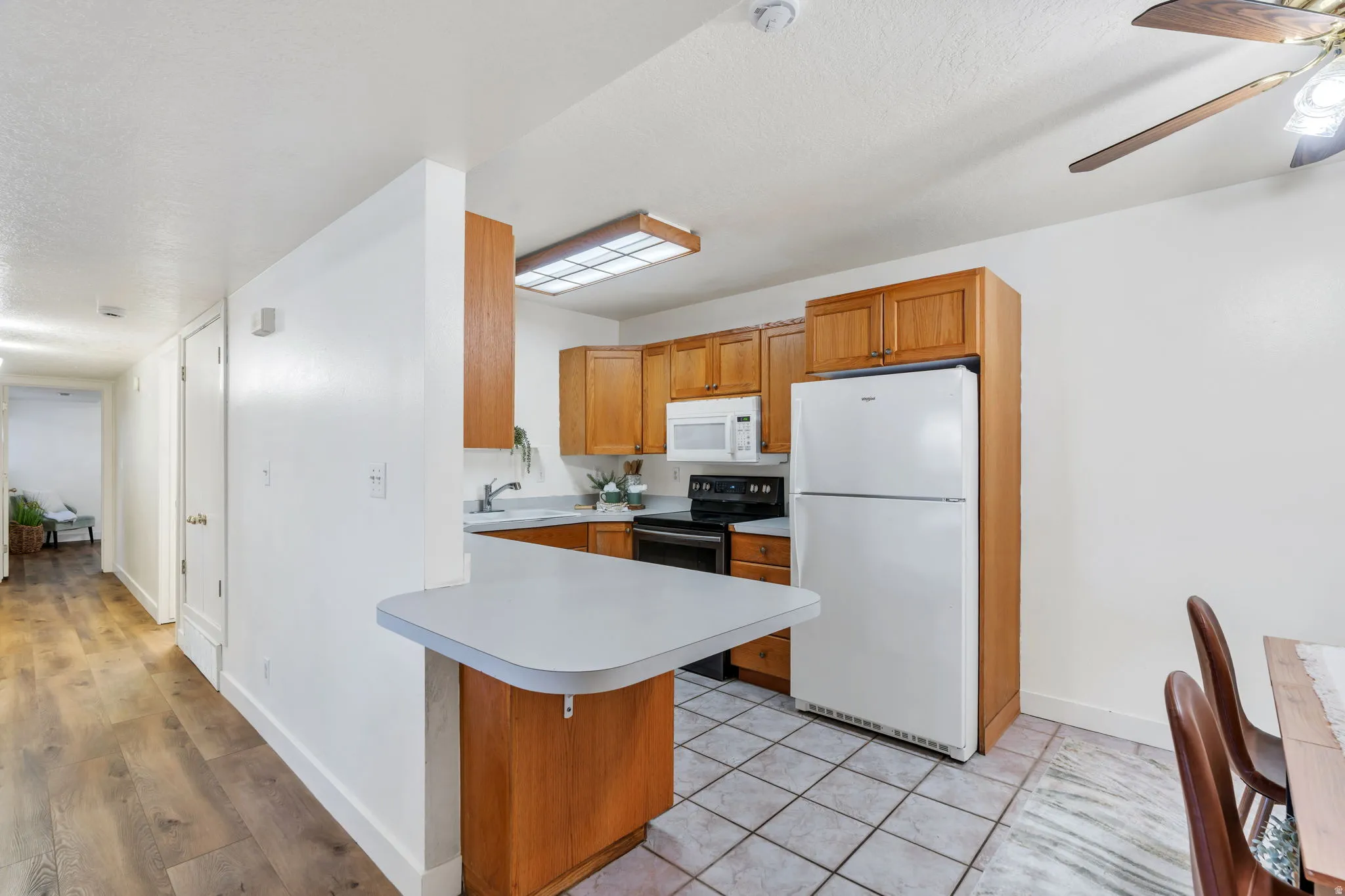 Kitchen featuring white appliances, wood finish cabinetry, light countertops, a peninsula, and a ceiling fan