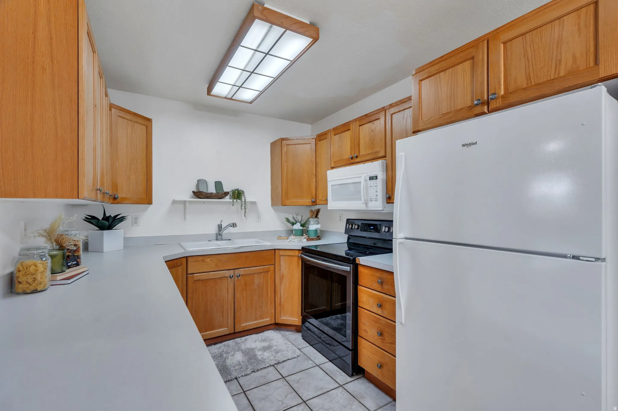 Kitchen featuring white appliances, light countertops, light tile patterned floors, and wood finish cabinetry