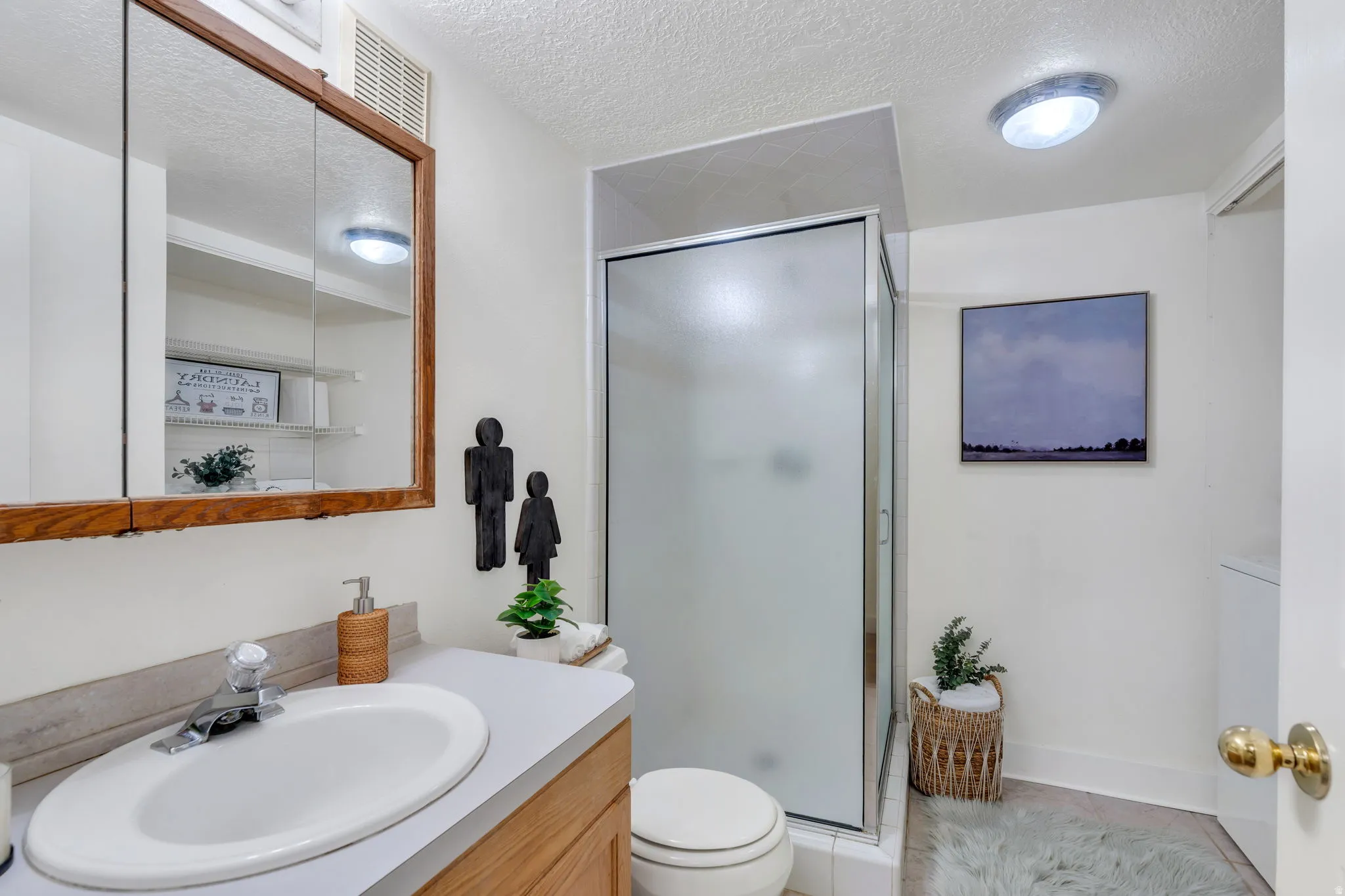 Full bath with a textured ceiling, vanity, a shower stall, light tile patterned floors, and washer / clothes dryer
