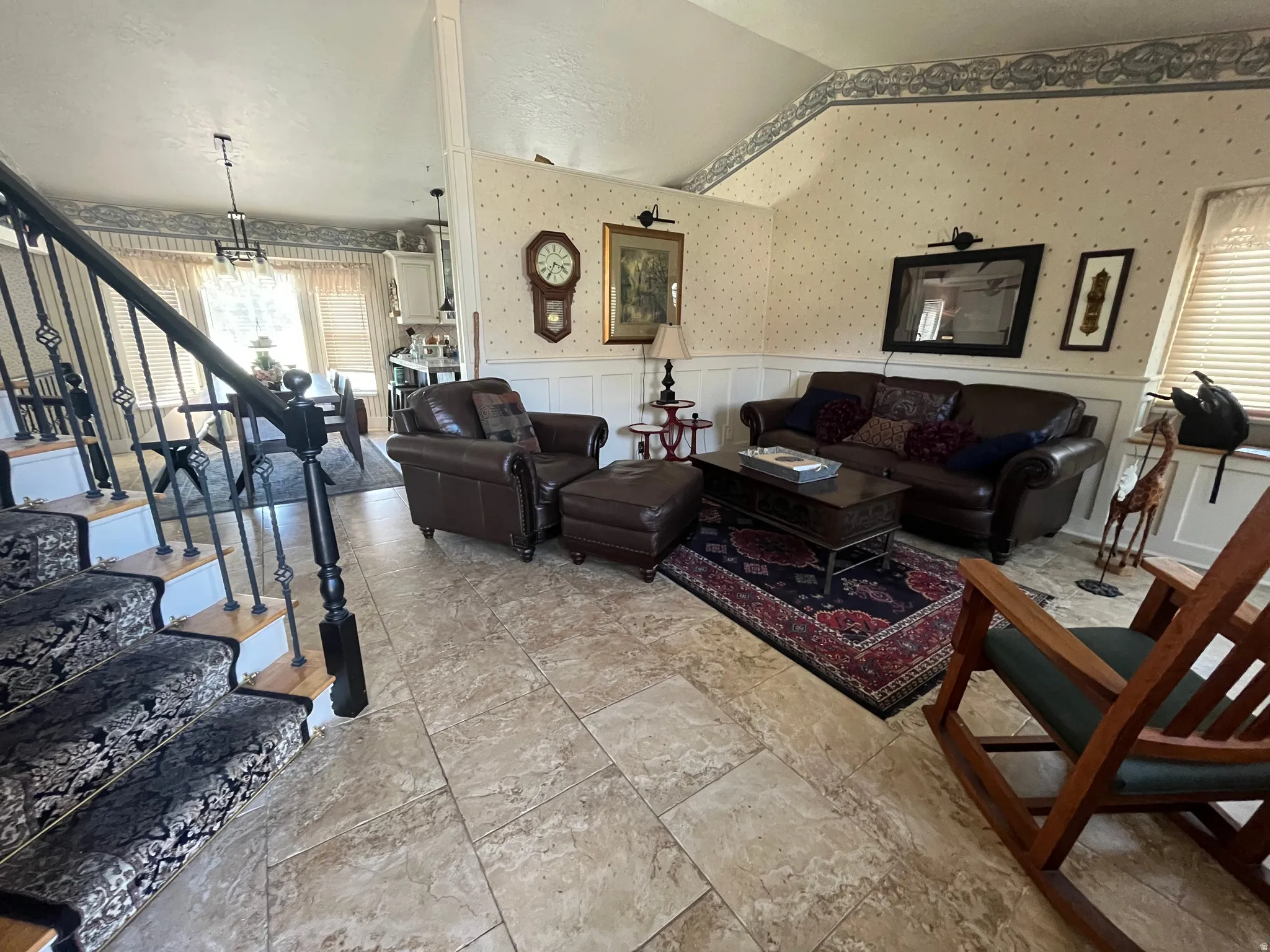 Living room with wallpapered walls, a wainscoted wall, hanging lights, lofted ceiling, and a decorative wall
