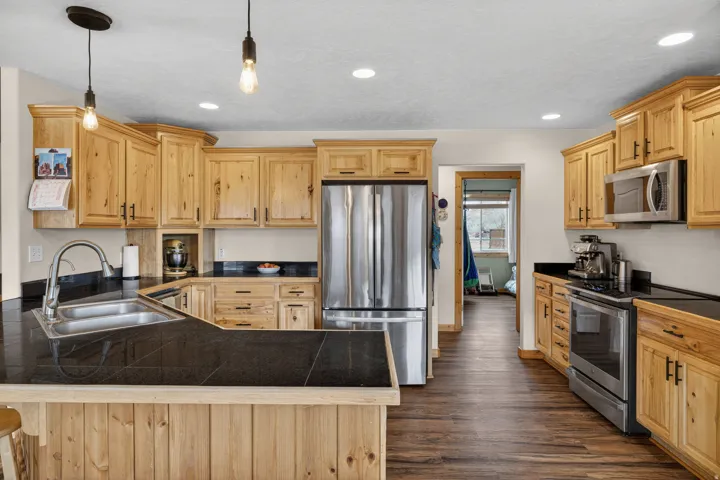 Kitchen with tile countertops, a peninsula, stainless steel appliances, light wood finish cabinets, and dark wood-type flooring