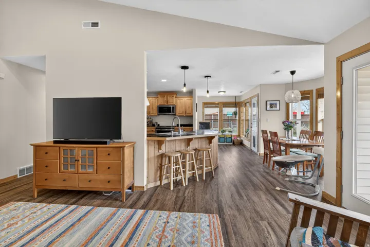 Kitchen with a breakfast bar area, dark wood-type flooring, lofted ceiling, decorative light fixtures, and stainless steel microwave