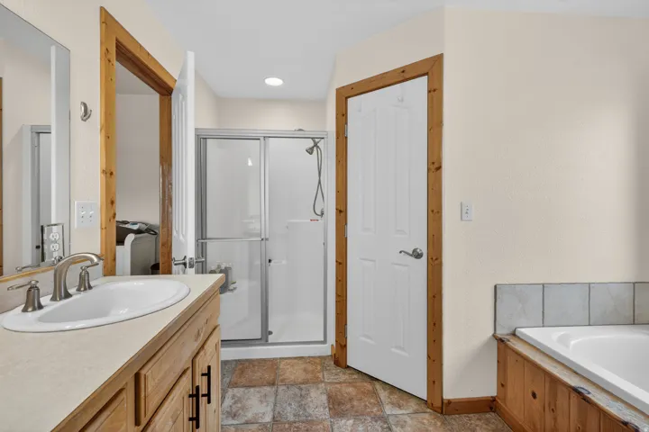 Bathroom featuring vanity, a shower stall, stone finish flooring, and a garden tub