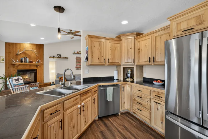 Kitchen featuring stainless steel appliances, decorative light fixtures, a large fireplace, a ceiling fan, and light wood finish cabinetry