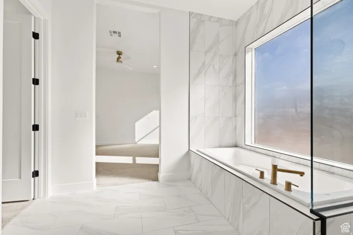 Bathroom featuring light marble finish flooring, a garden tub, and ceiling fan