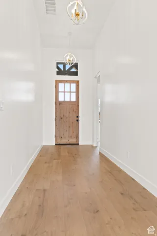 Entryway with suspended lighting, light wood finished floors, and a high ceiling