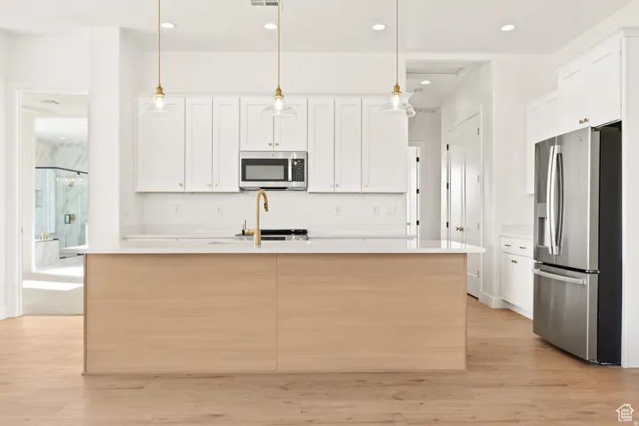 Kitchen featuring stainless steel appliances, light wood-type flooring, a center island with sink, and white cabinetry