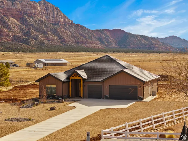 View of front facade featuring board and batten siding, driveway, a garage, and a view of countryside