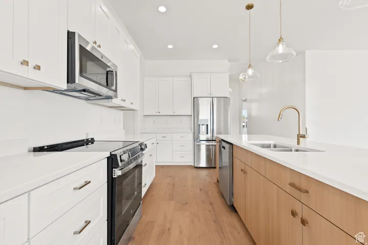 Two tone kitchen with stainless steel appliances, light wood-type flooring, pendant lighting, two tone color scheme, and light stone counters