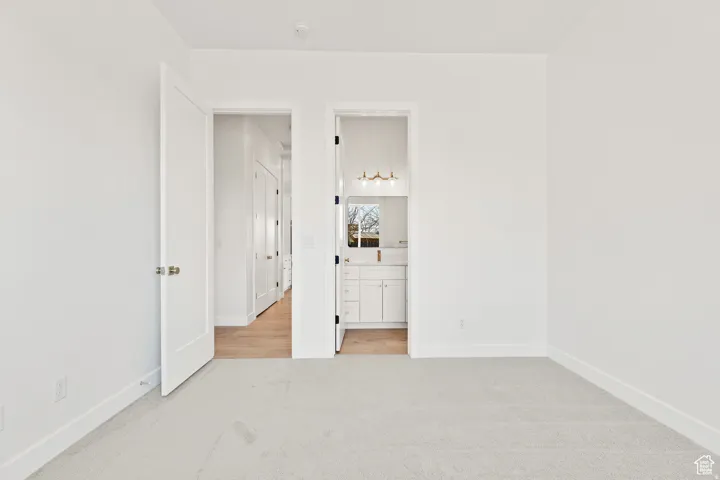 Unfurnished bedroom with light carpet and ensuite bath