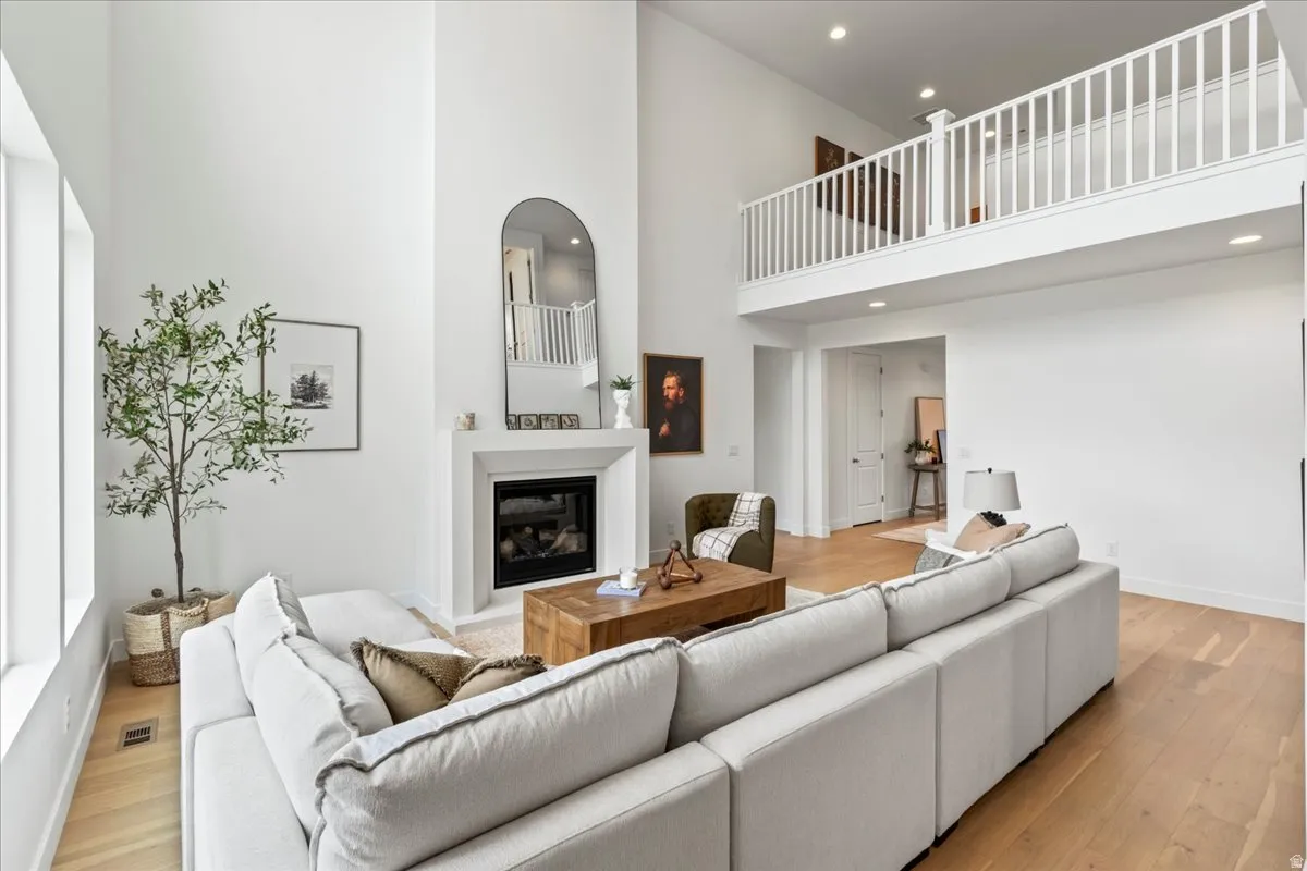 Living room with a high ceiling, light wood-type flooring, a glass covered fireplace, and recessed lighting